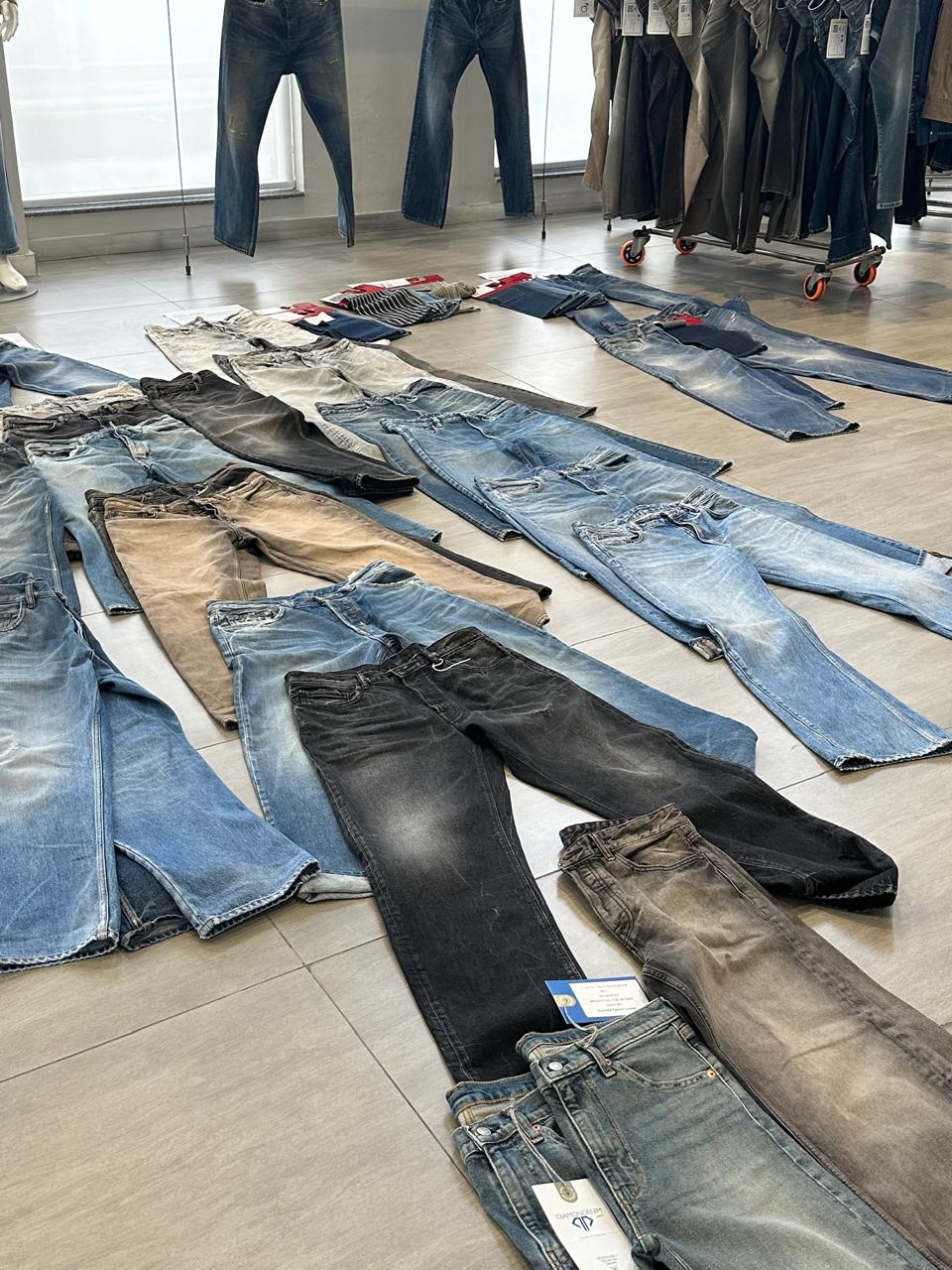 Diamond Denim by Sapphire showroom — 20+ denim garments laid out on the floor showing full collection range including light blue, black, grey, tan and distressed washes